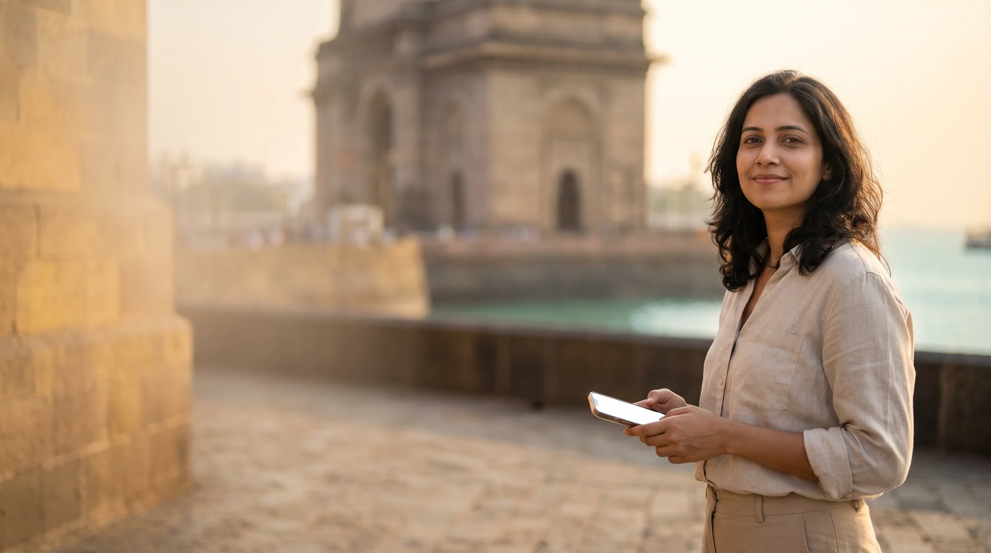 Traveler holding a phone at Gateway of India, Mumbai, in warm late-afternoon light